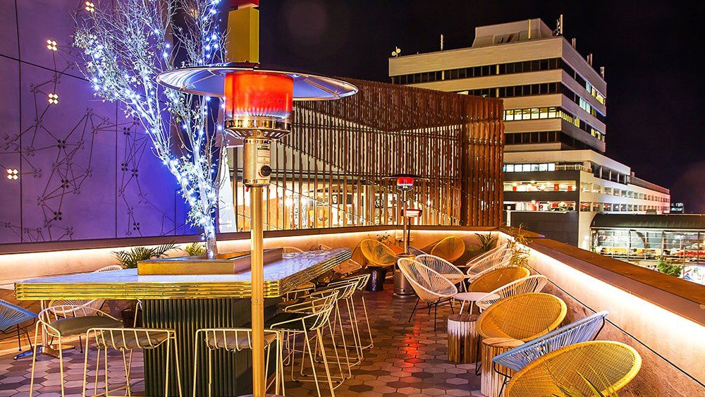 A rooftop bar with tables and chairs at night with a building in the background.