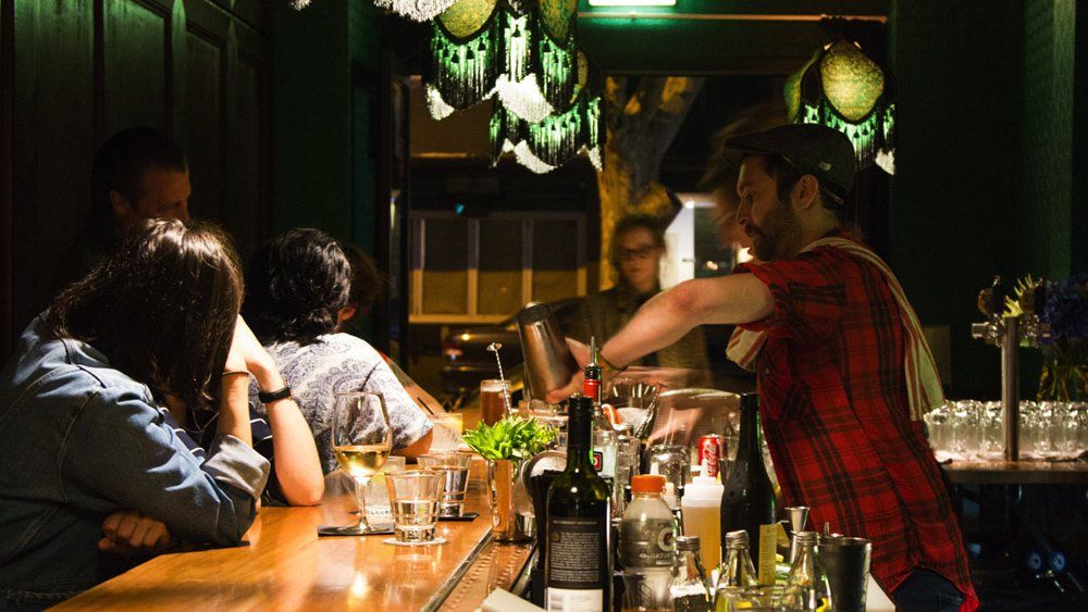 A bartender is preparing a drink for a group of people sitting at a bar.