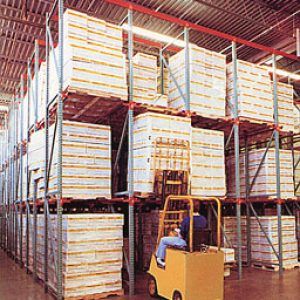 A man is driving a forklift in a warehouse filled with lots of boxes.