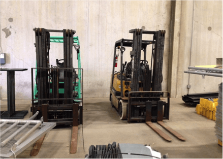Two forklifts are parked next to each other in a warehouse