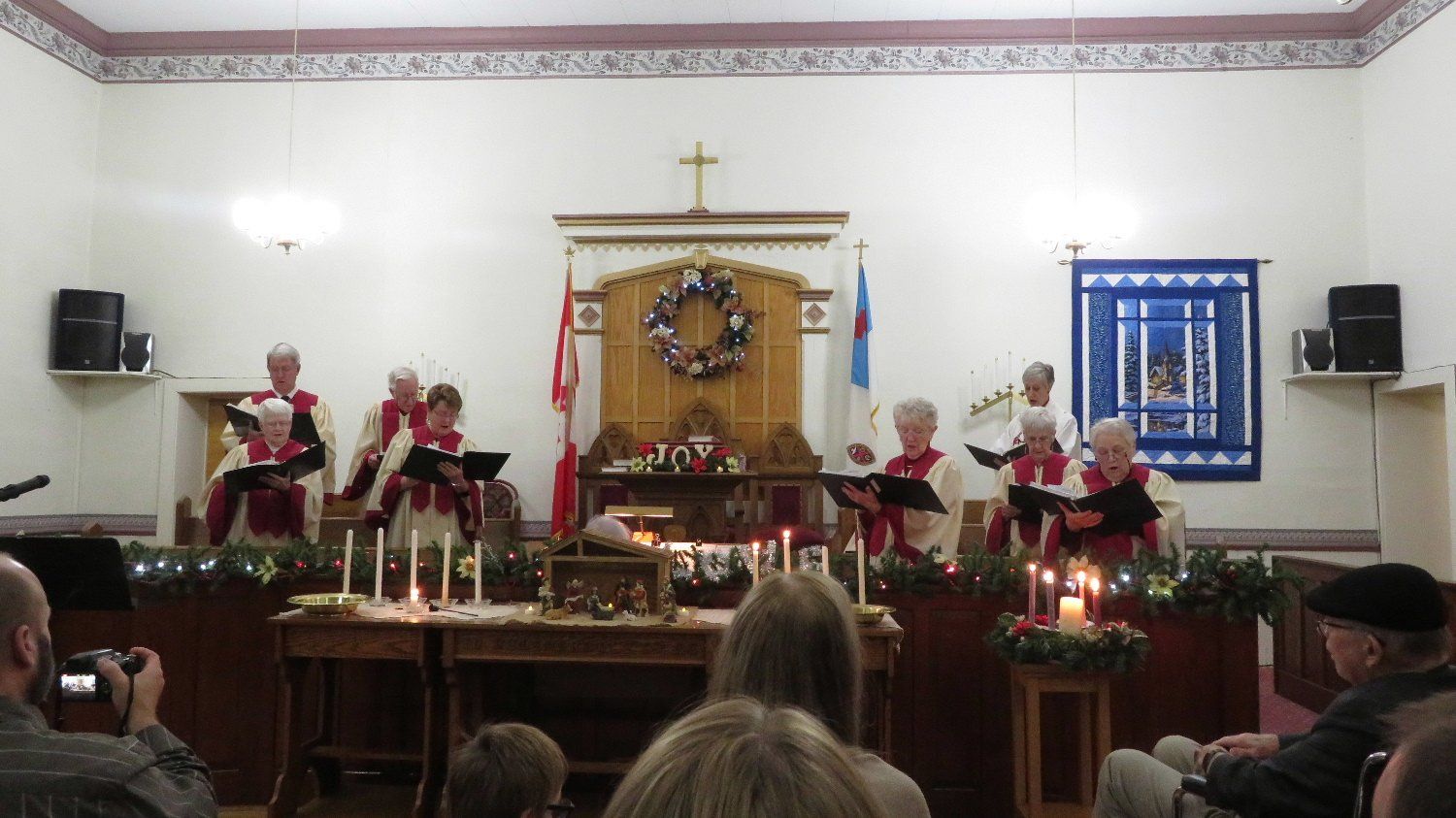 Church choir performing at the altar, with candles, flowers, and congregation seated in the foreground