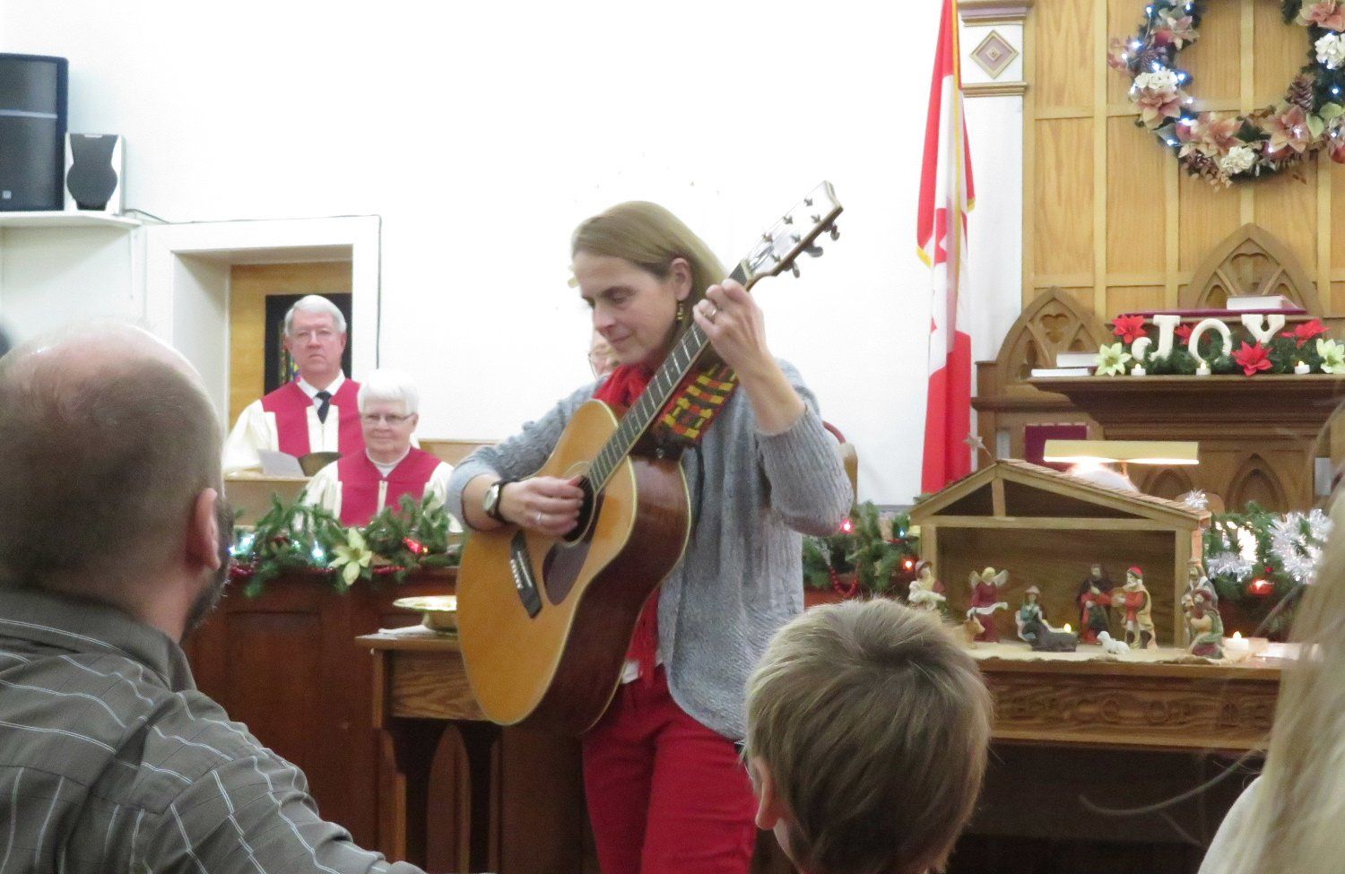 Woman playing guitar at a church service, with an altar and seated audience in the background