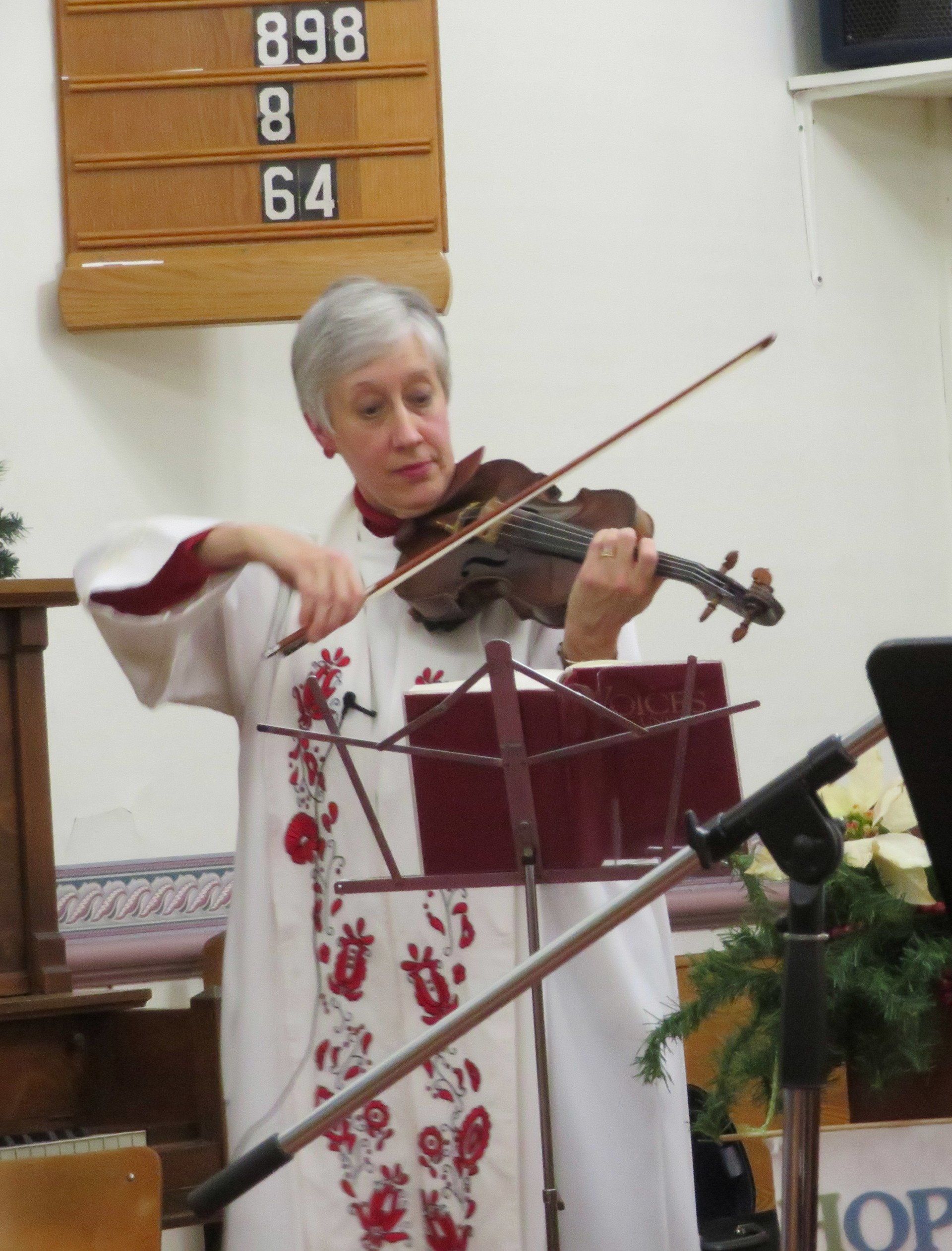 Woman playing violin in a church, standing behind a music stand and microphone.