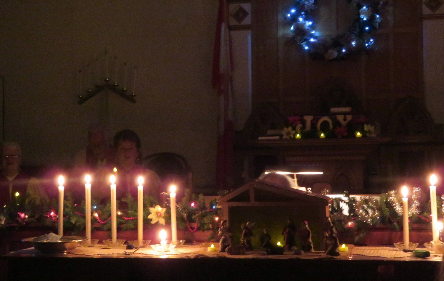 A candlelit dining table with a decorated centerpiece and two people seated in a dim room