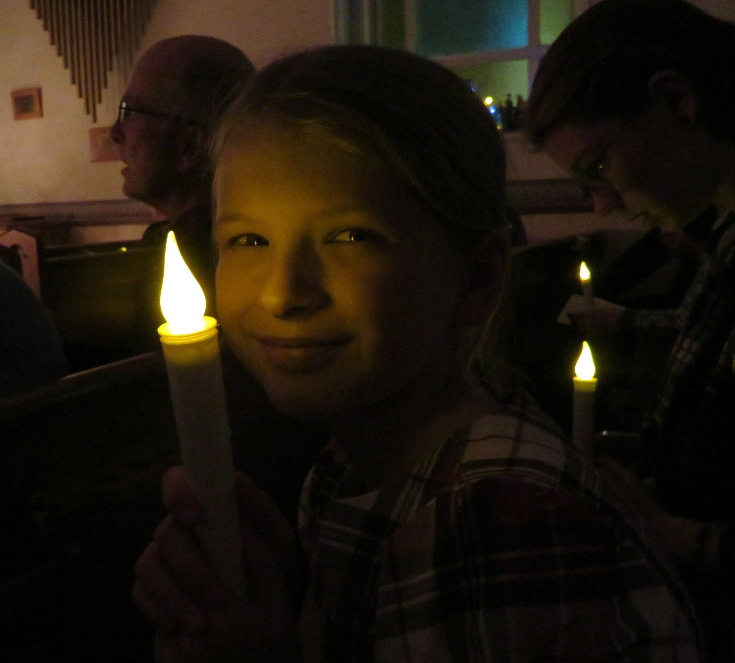 Child smiling and holding a lit candle in a dim room during a candlelight event