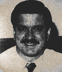 Black-and-white portrait of a man in a white shirt and tie, smiling at the camera.