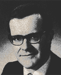 Black-and-white portrait of a man wearing glasses and a suit, looking at the camera with a slight smile.
