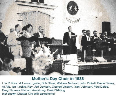 Men’s choir performs at church with conductor, pianist, and flower arrangement in front of pulpit.