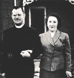 Two people standing outside a building, one in dark clothing and one in a light suit.