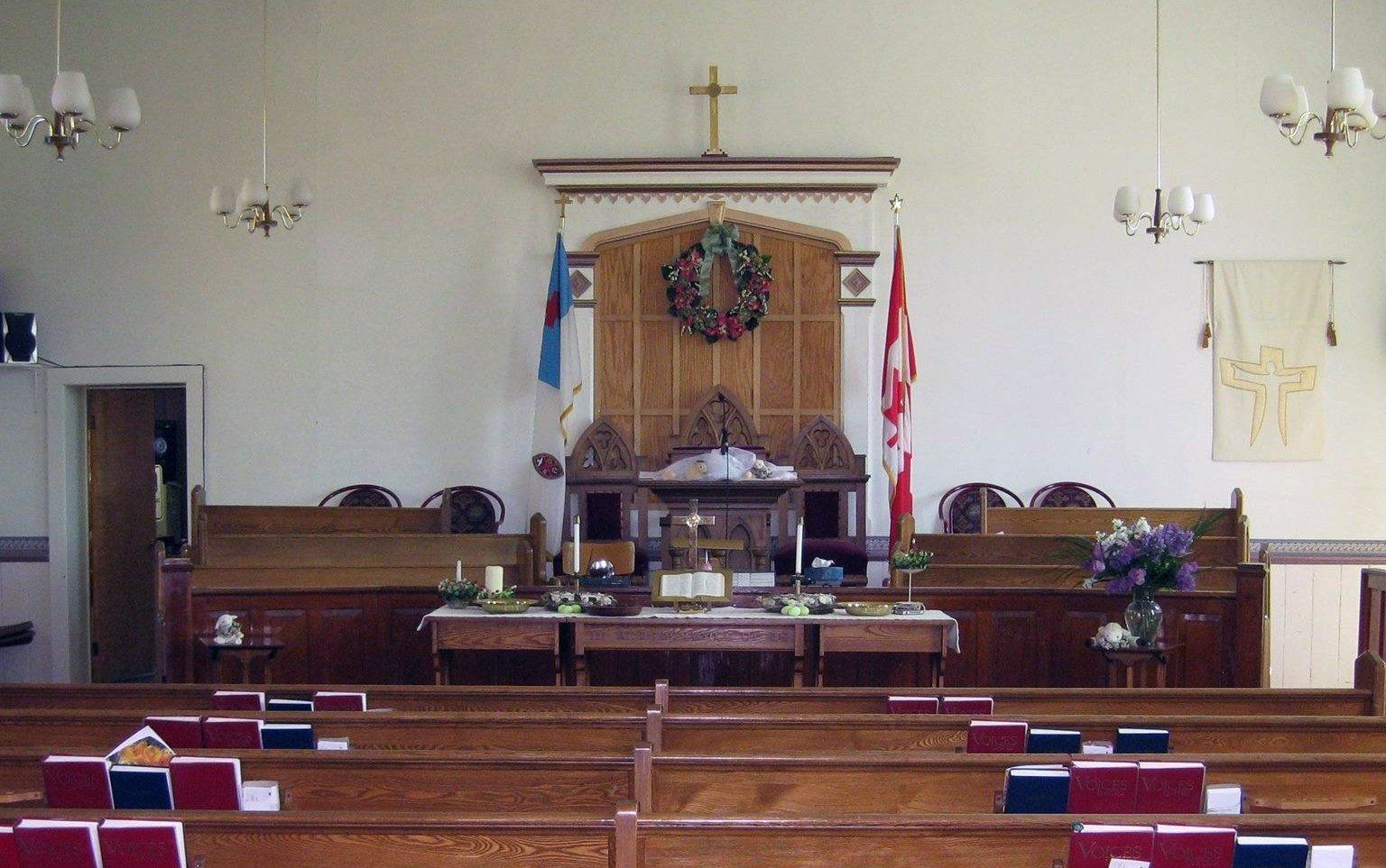 Empty church sanctuary with altar, pews, crucifix, and flags at the front