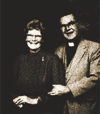 Two people posing together, one in dark clothing and one in a light jacket, smiling at the camera.