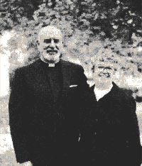 Two people standing outdoors, one in a clerical collar, in a black-and-white photo.