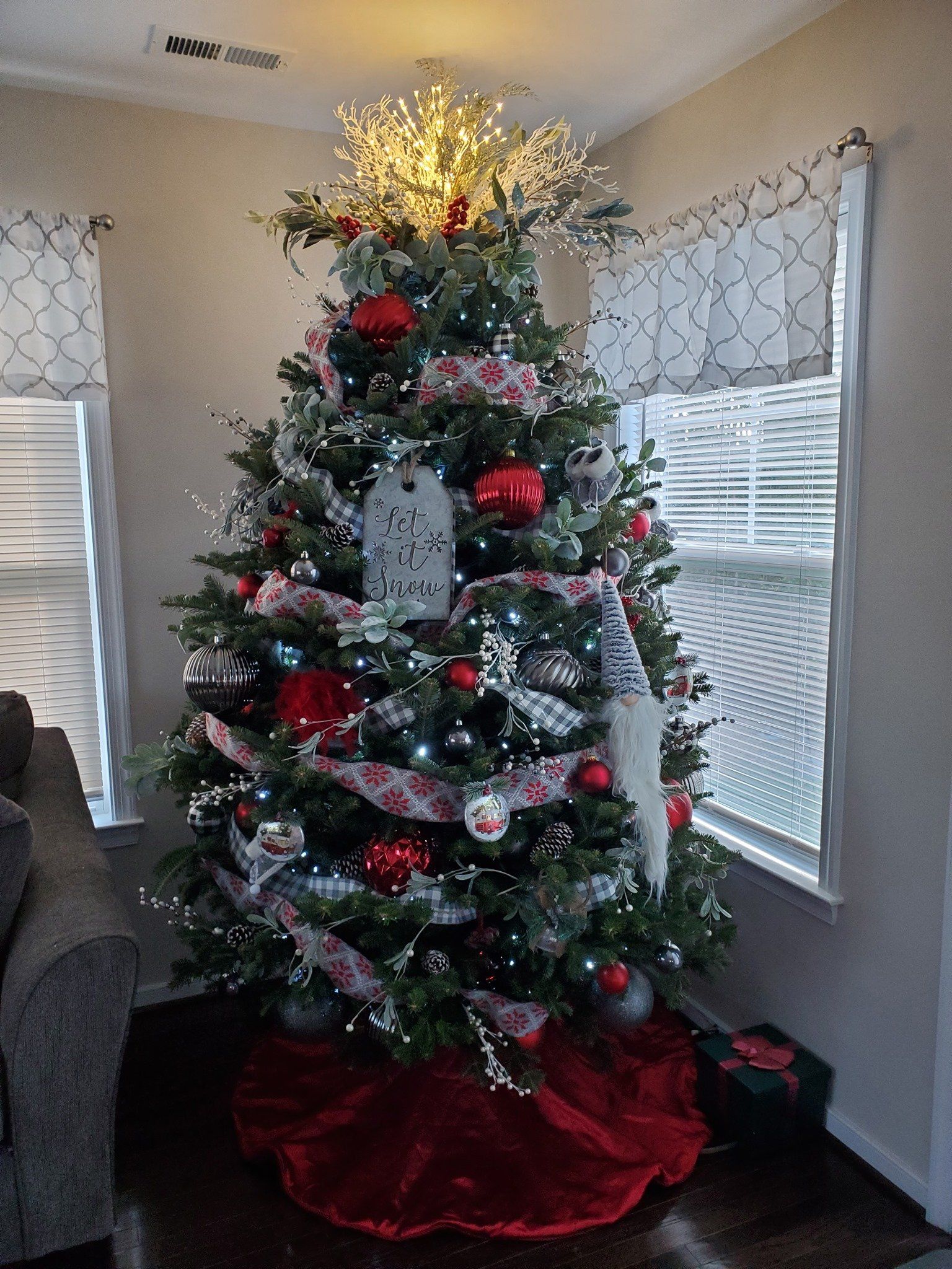 A christmas tree is sitting in a living room next to a window.
