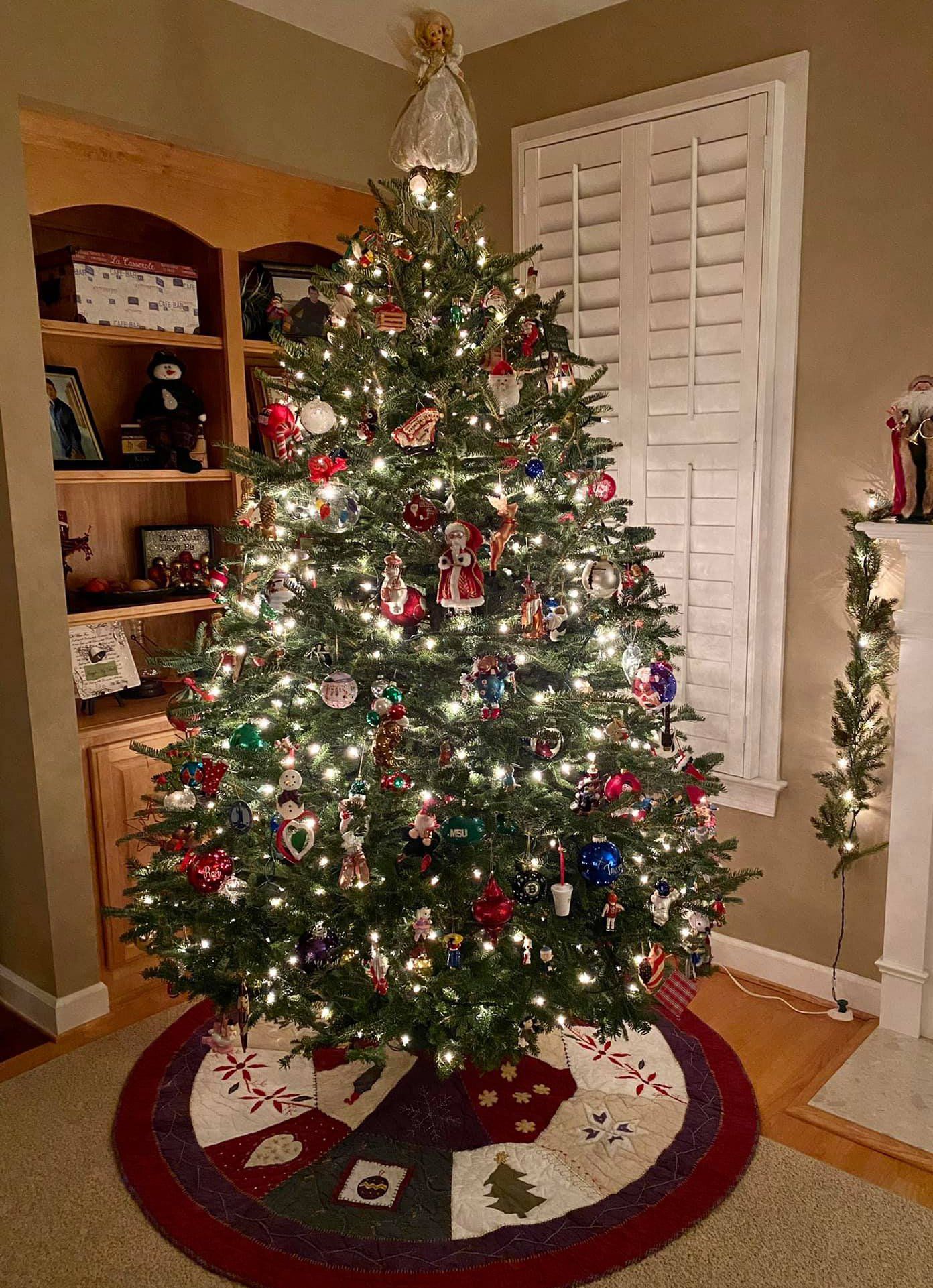 A christmas tree is sitting in a living room next to a fireplace.