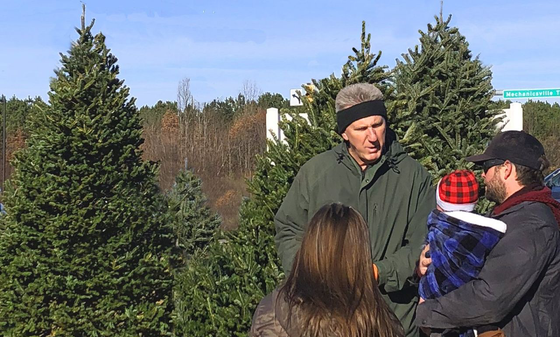 A group of people are standing in front of a christmas tree farm.