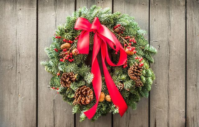 A christmas wreath with a red bow is hanging on a wooden wall.