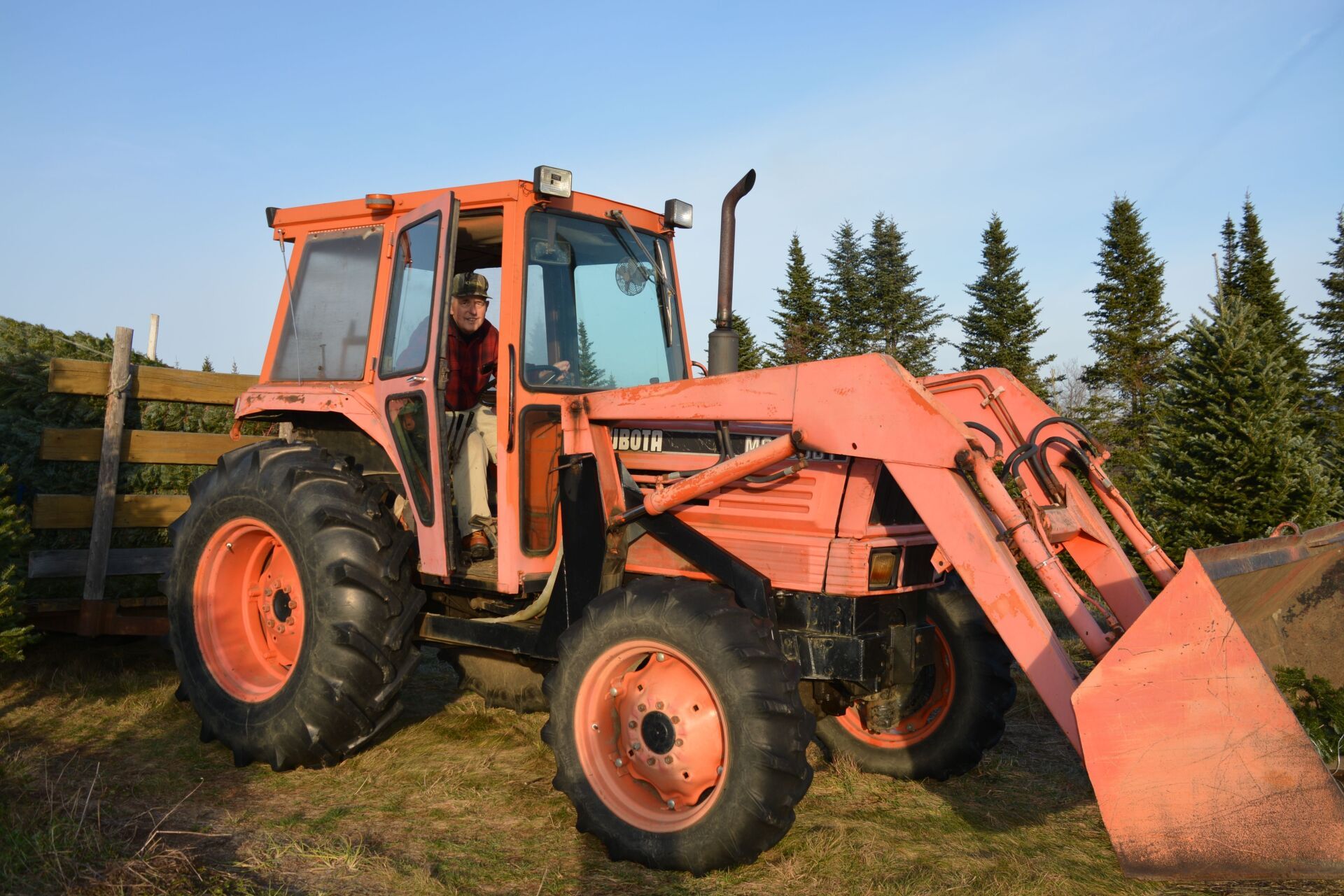A man is sitting in the driver 's seat of an orange tractor.