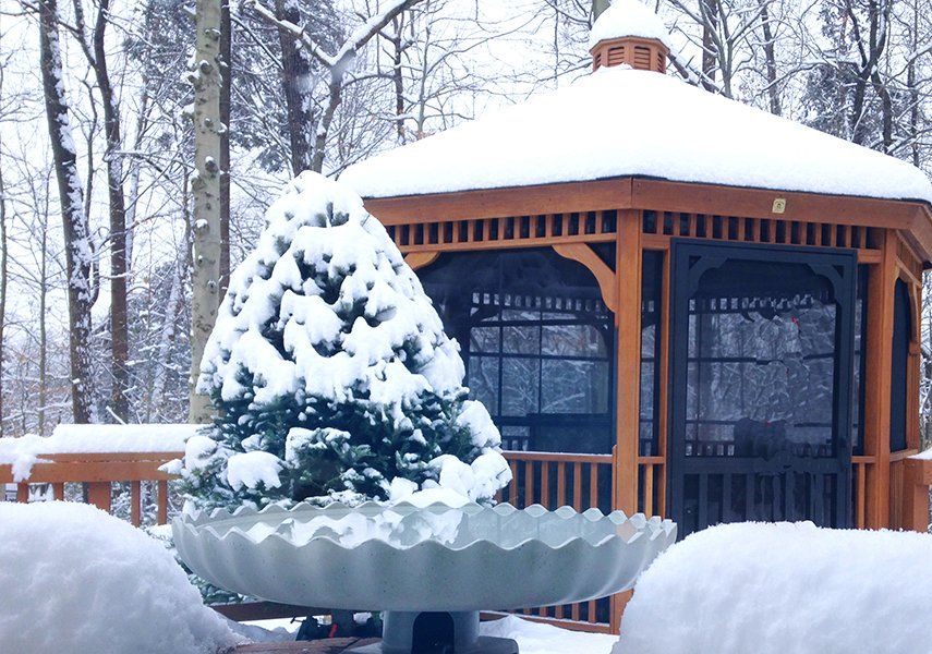 A gazebo covered in snow with a tree in the foreground