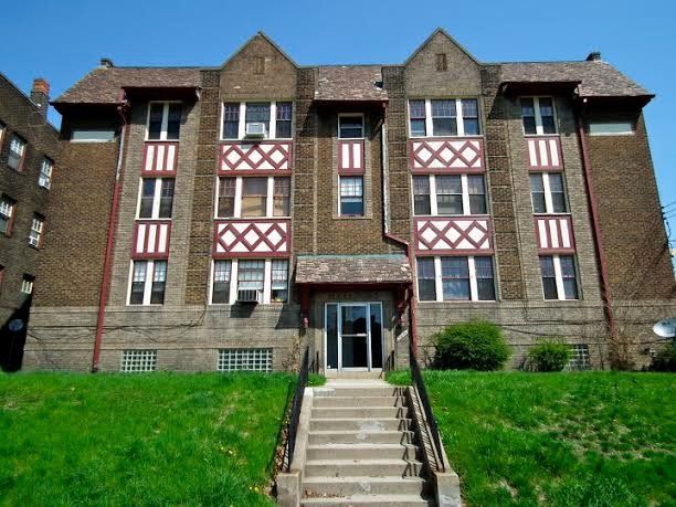 Apartment building with red and white details, stone facade, and a staircase leading to the entrance.