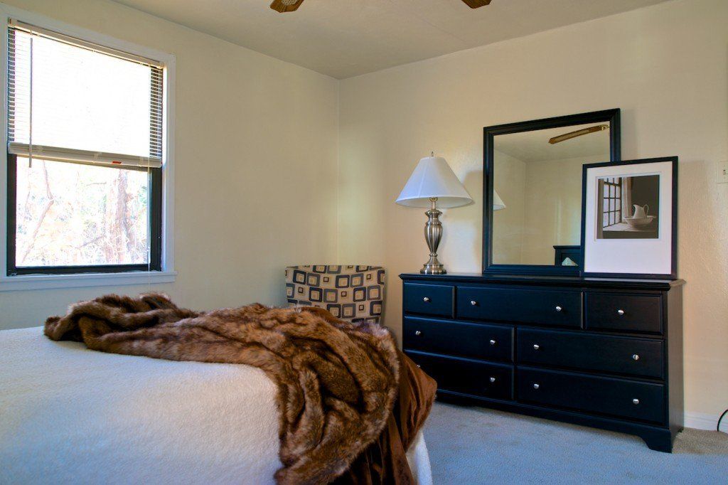 Bedroom with a bed, black dresser with mirror, window, and a patterned chair.