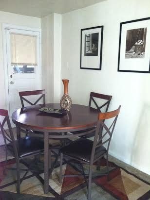 Dining table with four chairs, vase, art, and a door in a bright corner.