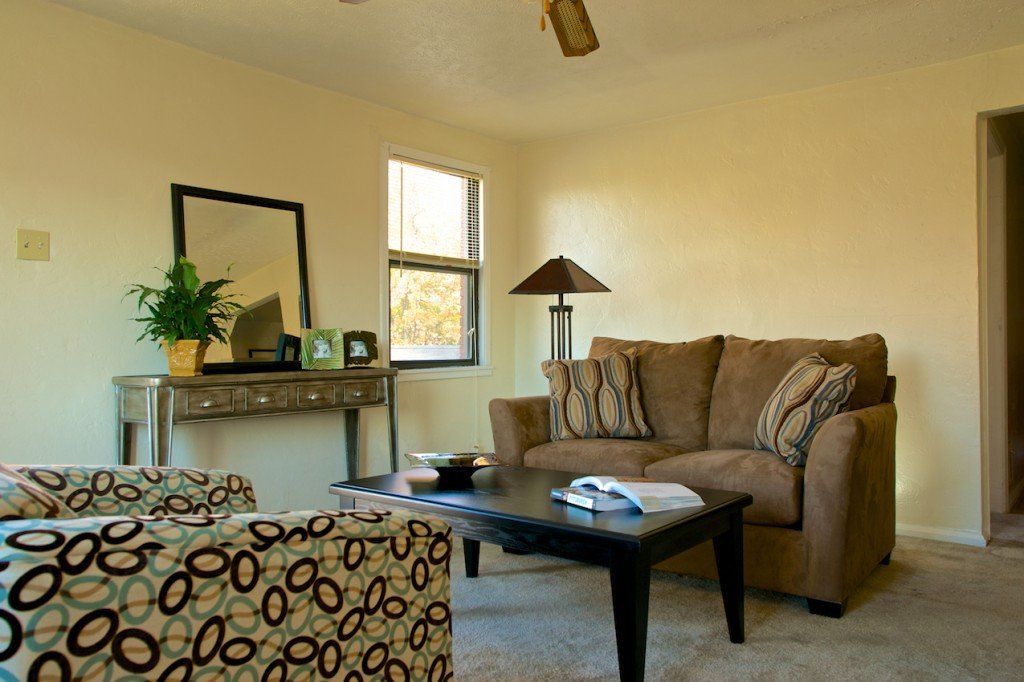 Living room with brown couch, patterned armchair, table, mirror, and window.