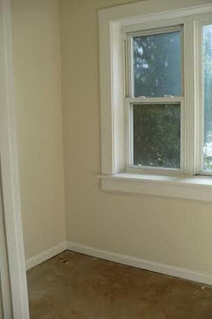 Empty room with a window; beige walls, white trim, and stained floor.