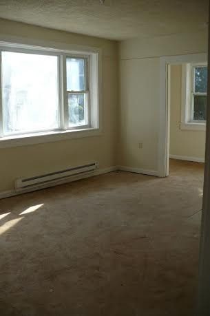 Empty room with two windows, beige walls, brown carpet, and a doorway to another room.