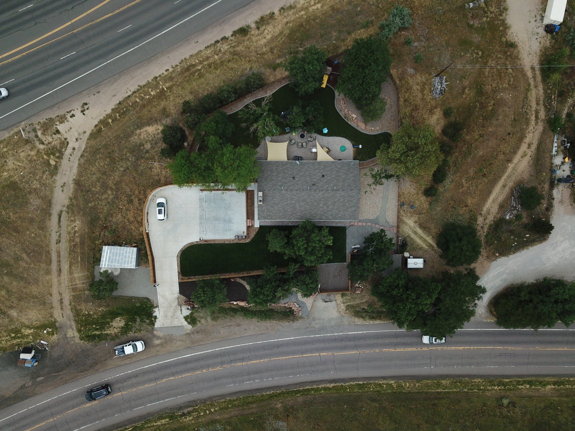 Aerial view of a house with a driveway and surrounded by vegetation, near a road.