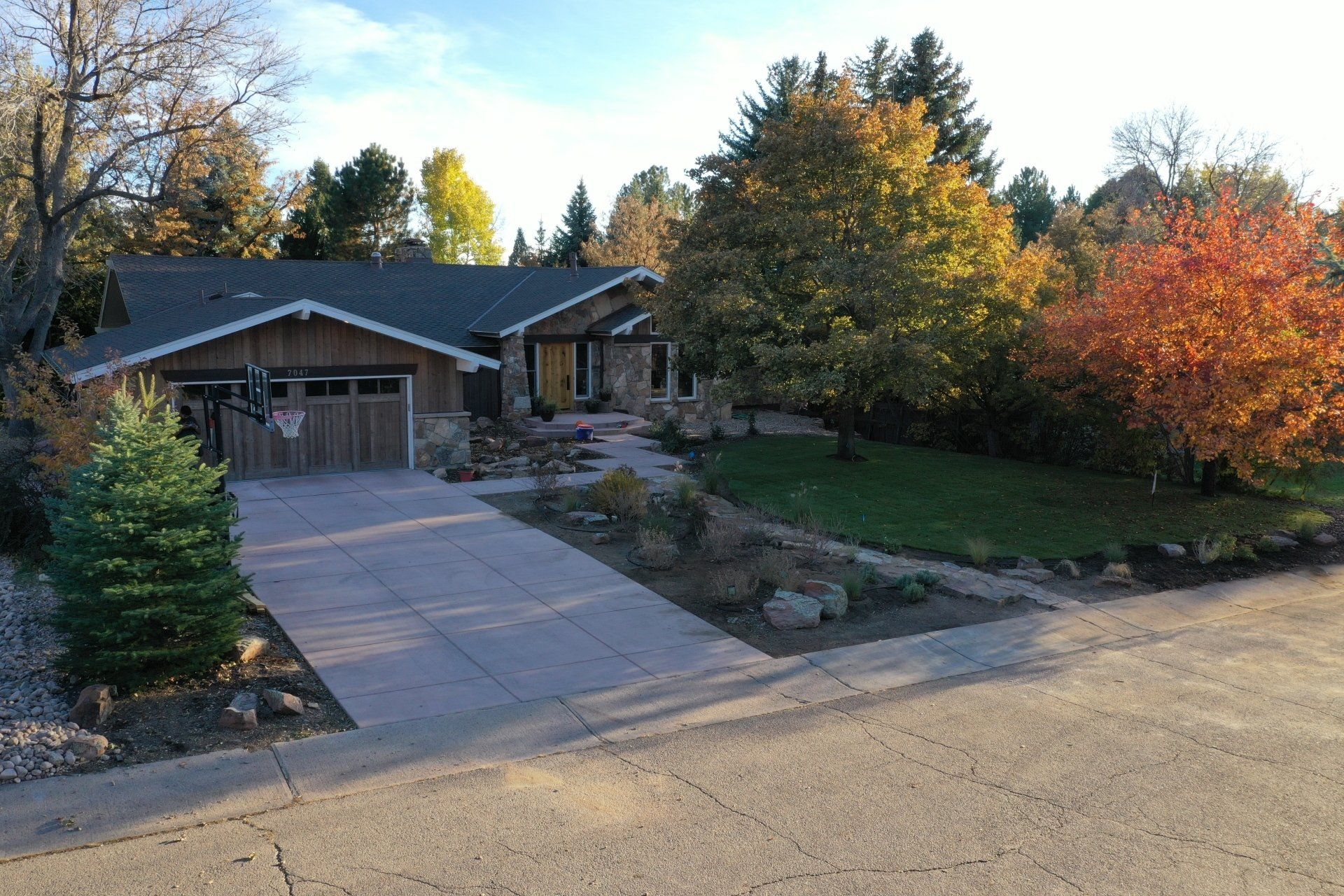 House with brown siding and garage, driveway, and colorful autumn trees.