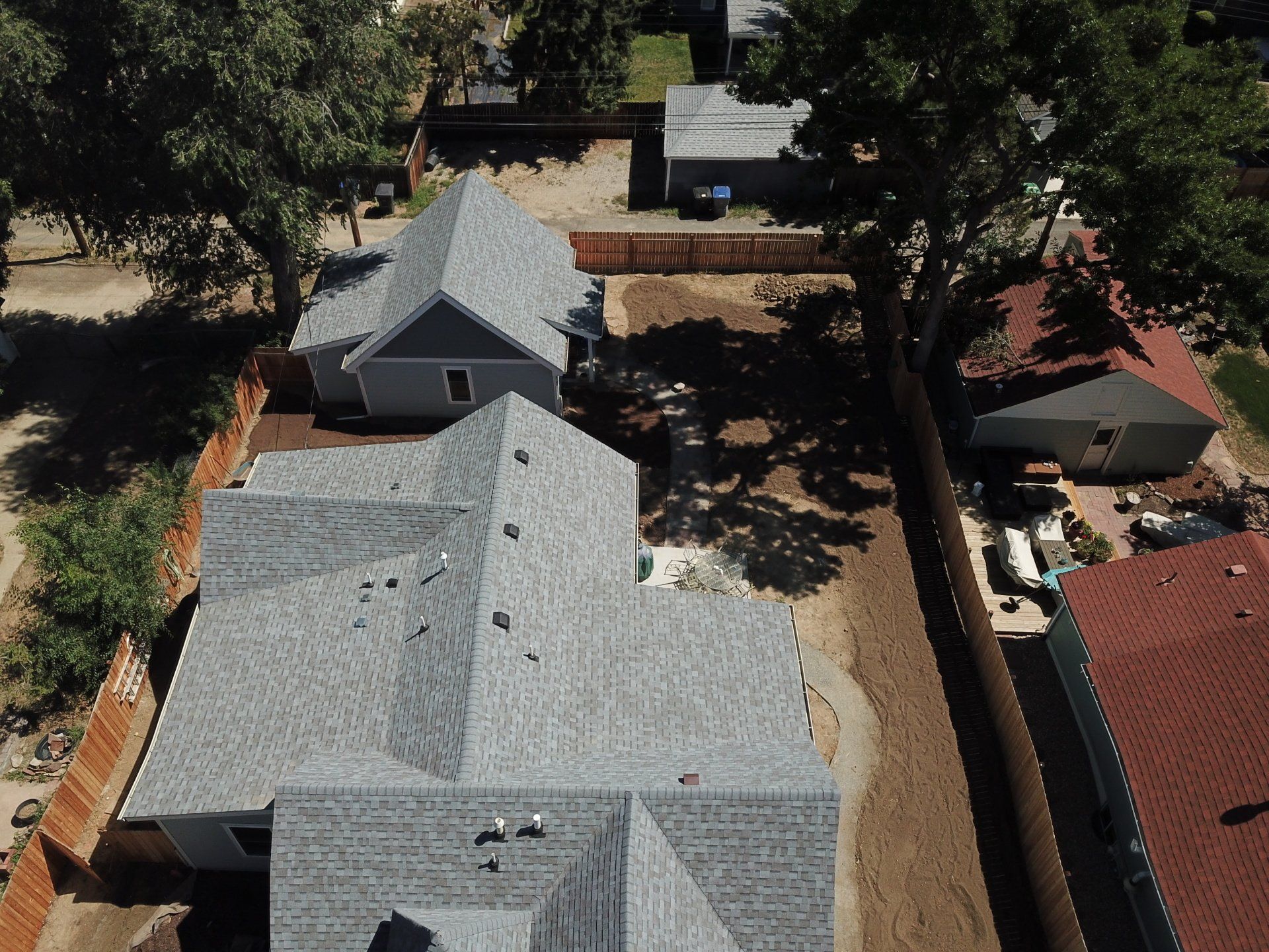 Aerial view of two houses with gray roofs, brown fences, and a tree, sunny day.