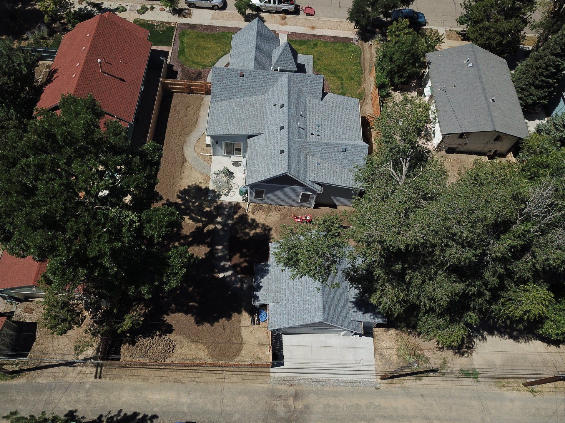 Aerial view of a gray-roofed house with a light gray driveway; trees and neighboring houses are visible.