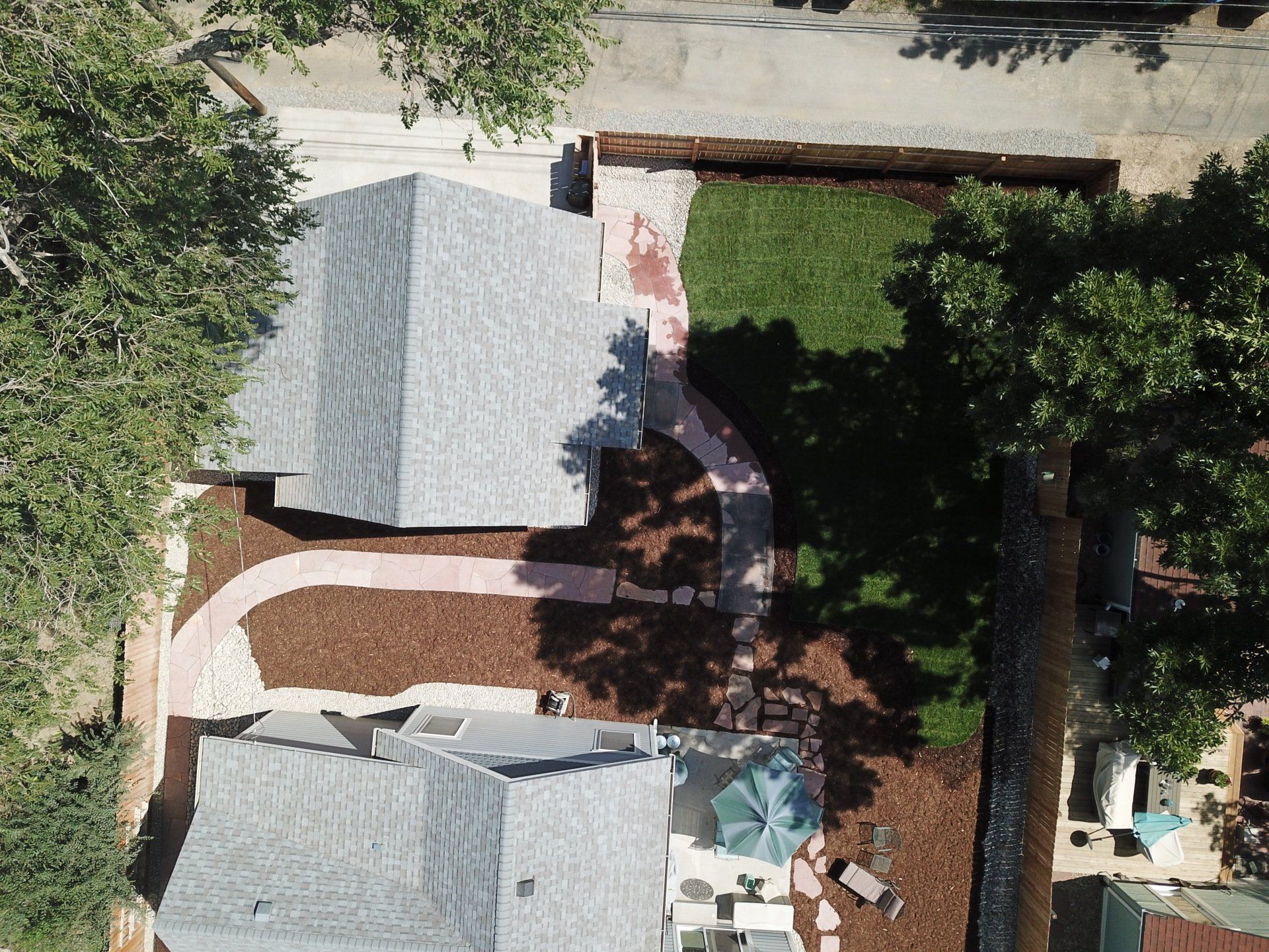 Overhead view of two houses with grey roofs, connected by a winding red brick path in a yard with grass and mulch.