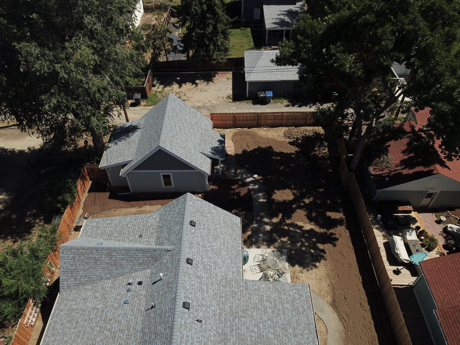 Aerial view of two houses with gray roofs and a brown wooden fence, surrounded by trees.