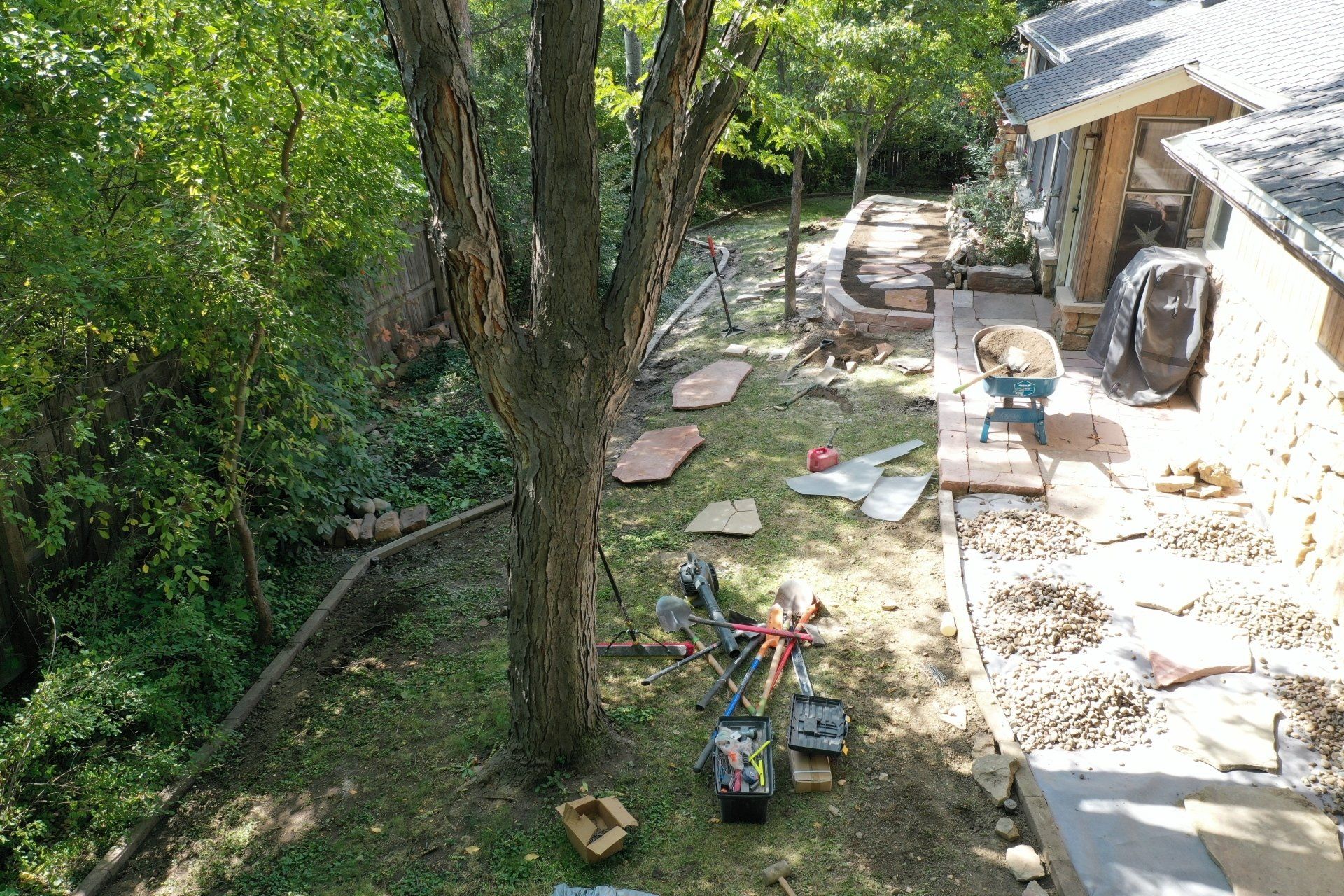 Backyard landscape construction site with tools, a tree, and stone pathway.