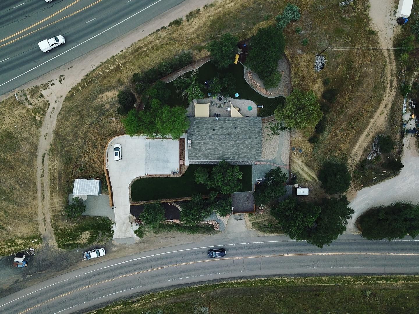 Overhead view of a house next to a road and highway. Cars are driving on the road.