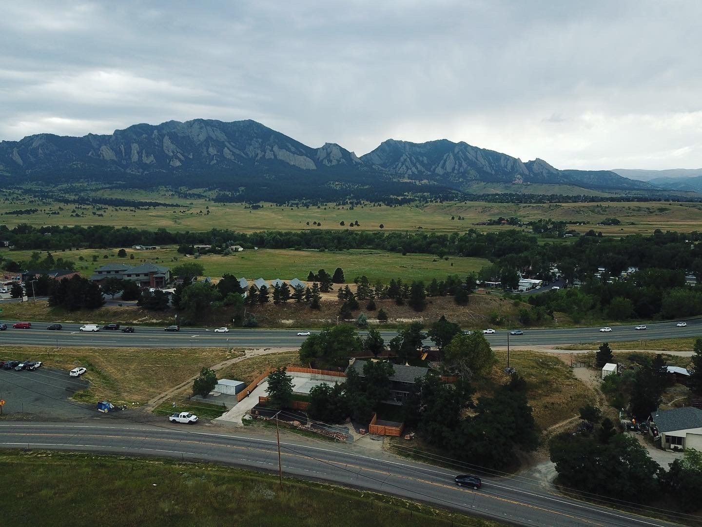 Mountains loom over a valley, highway, and structures. Overcast sky.