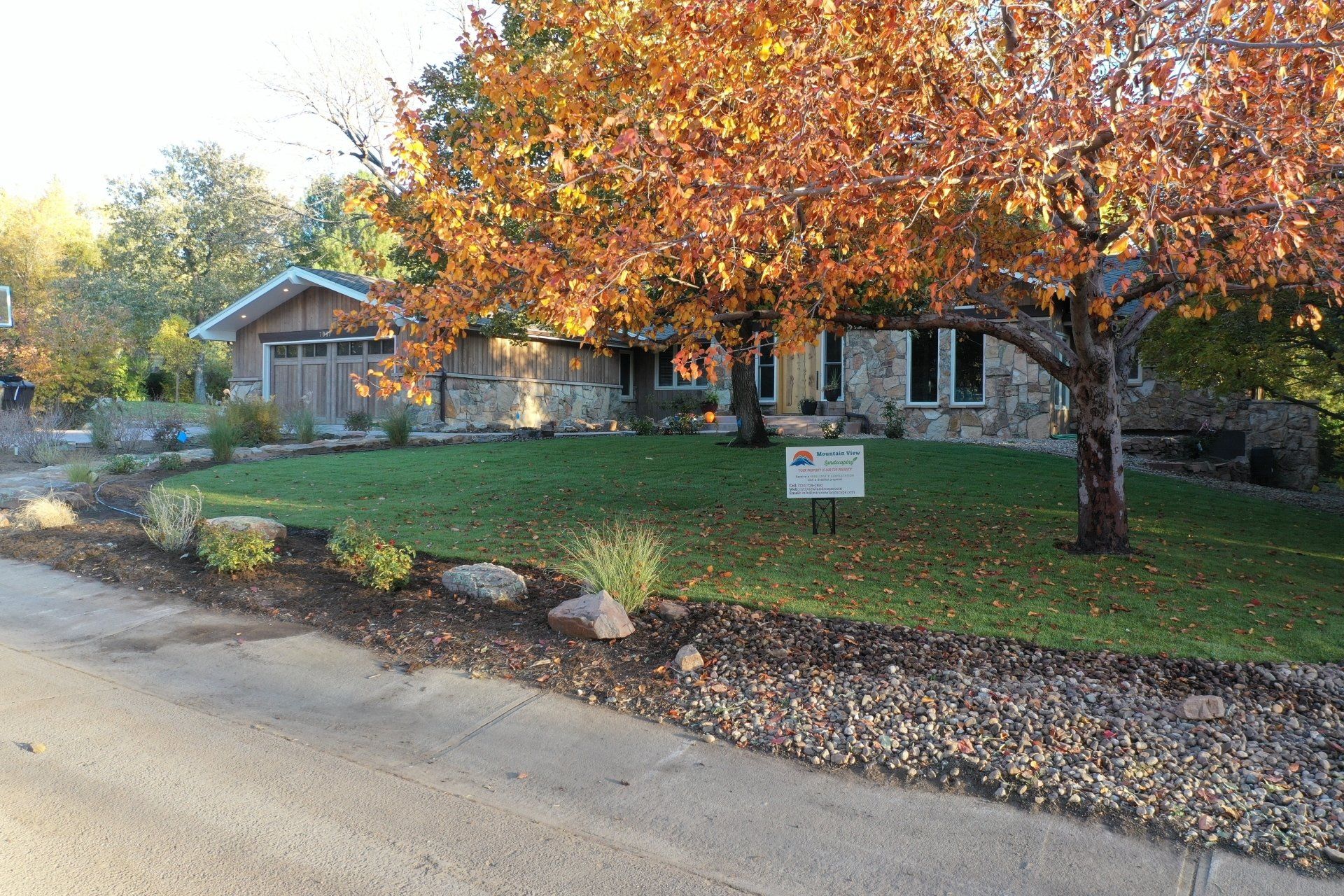 Stone house with fall foliage, green lawn, and sign in front.