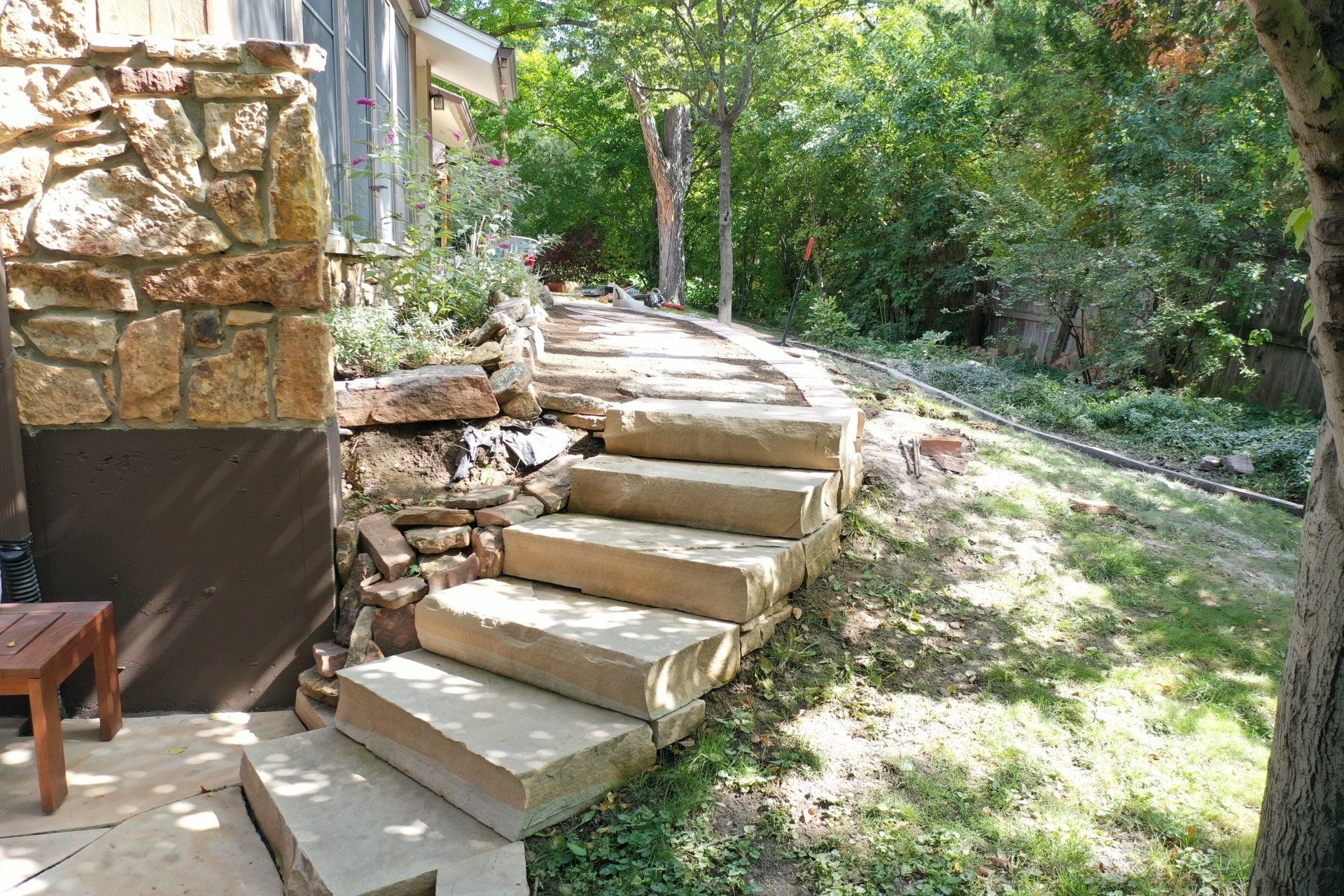 Stone steps leading uphill in a garden, next to a stone building and lush greenery.