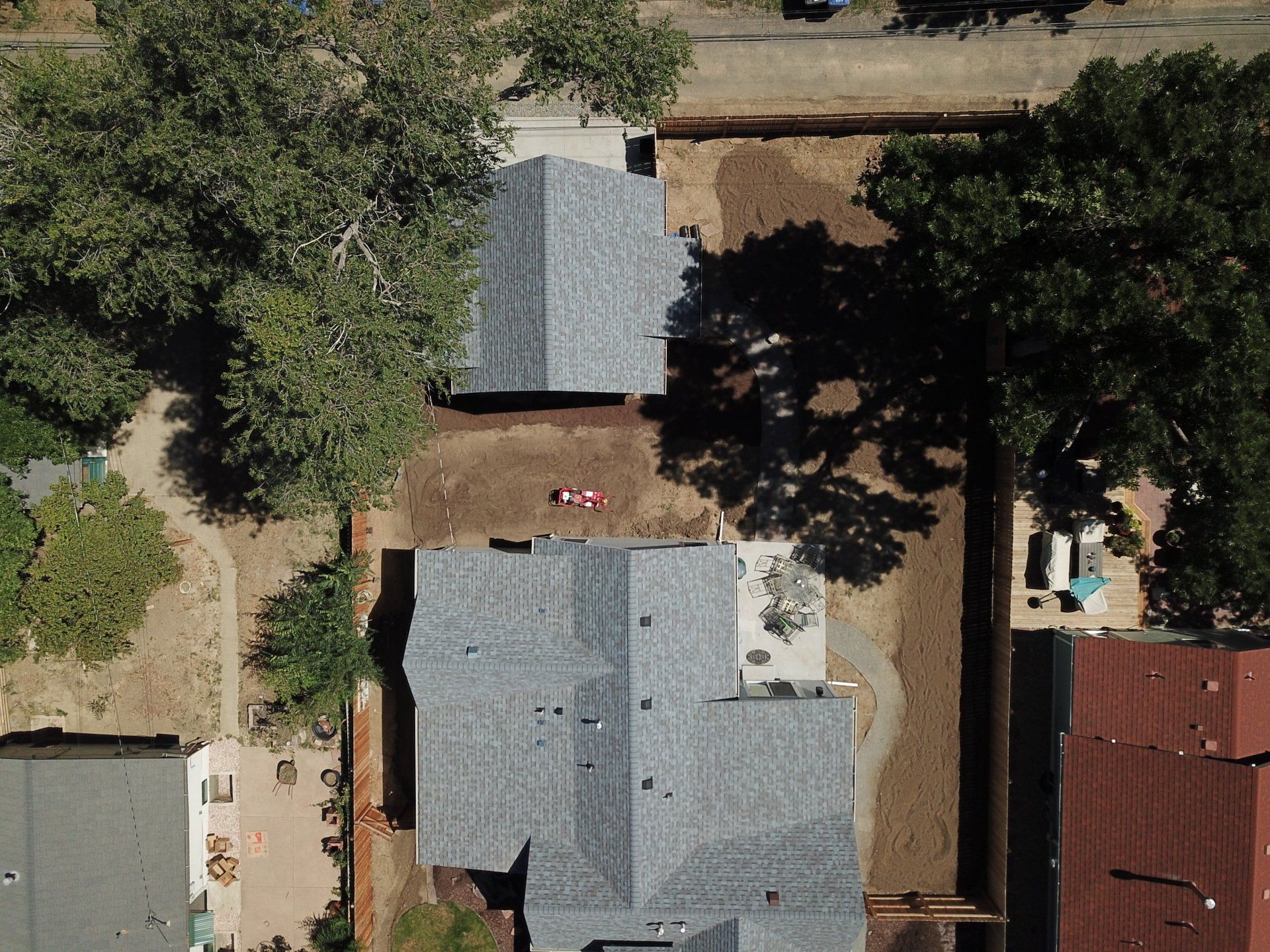 Overhead view of homes, trees, and construction, featuring gray rooftops and brown earth.