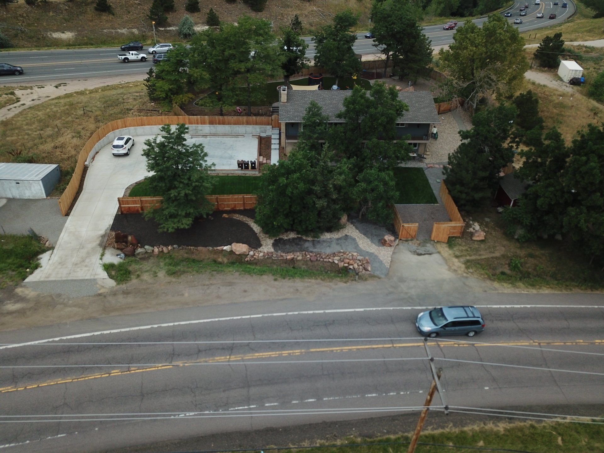 An aerial view of a house next to a road, with a driveway and cars visible.