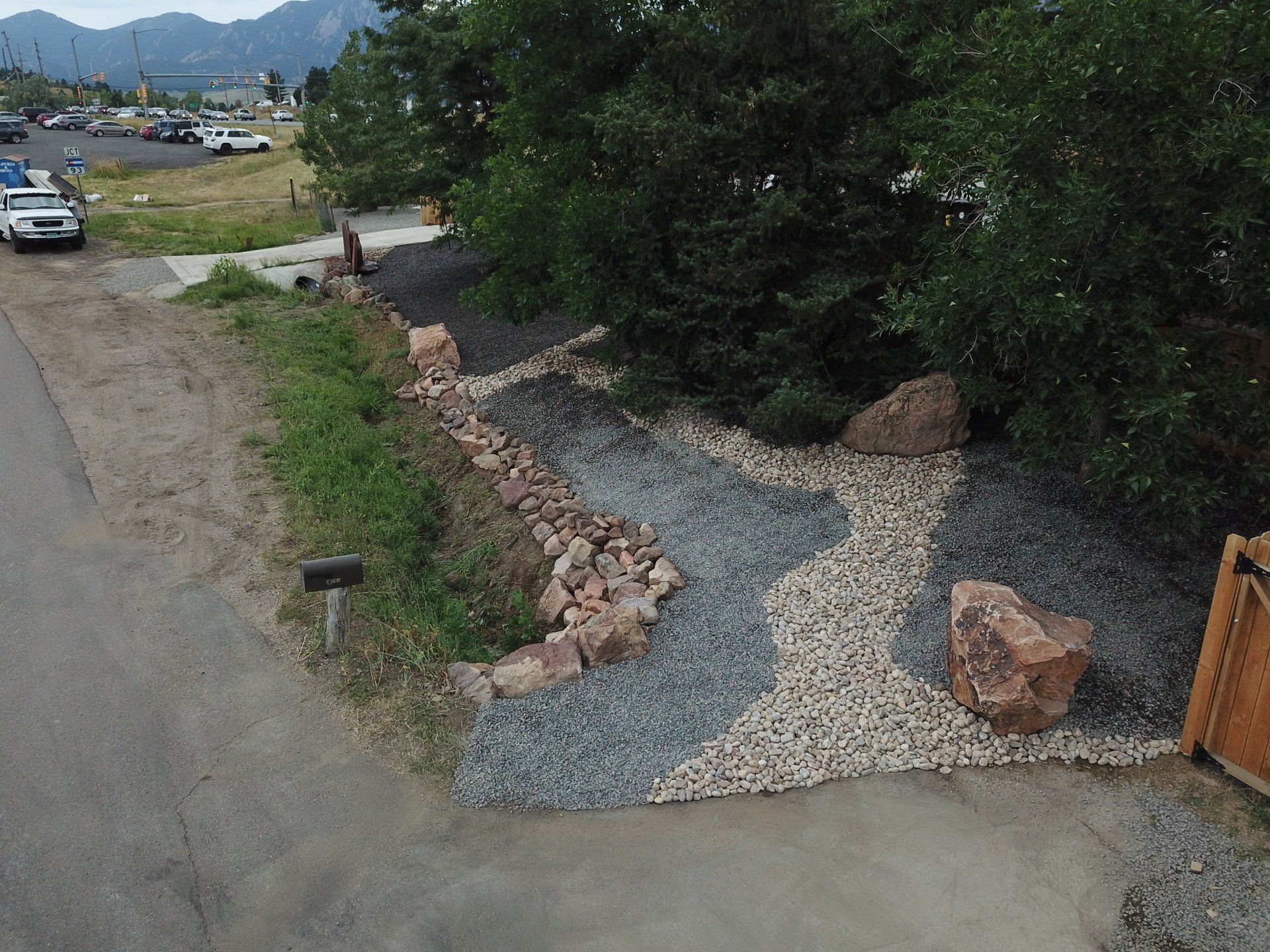 Landscape with rock and gravel paths, trees, and mountains in the background. A mailbox is visible.