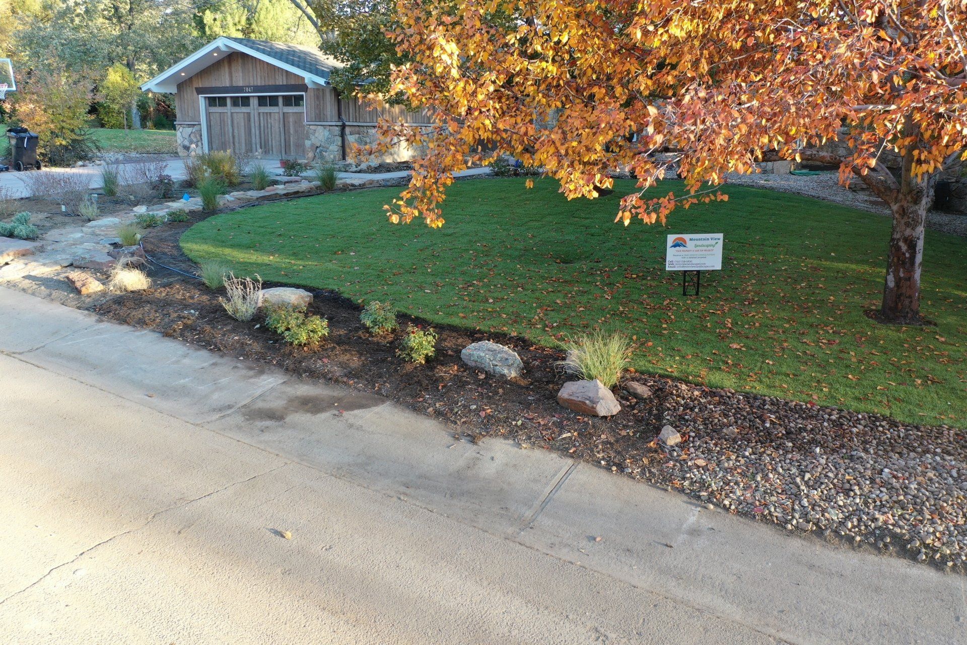 A house with a small lawn, mulch, and colorful fall foliage.