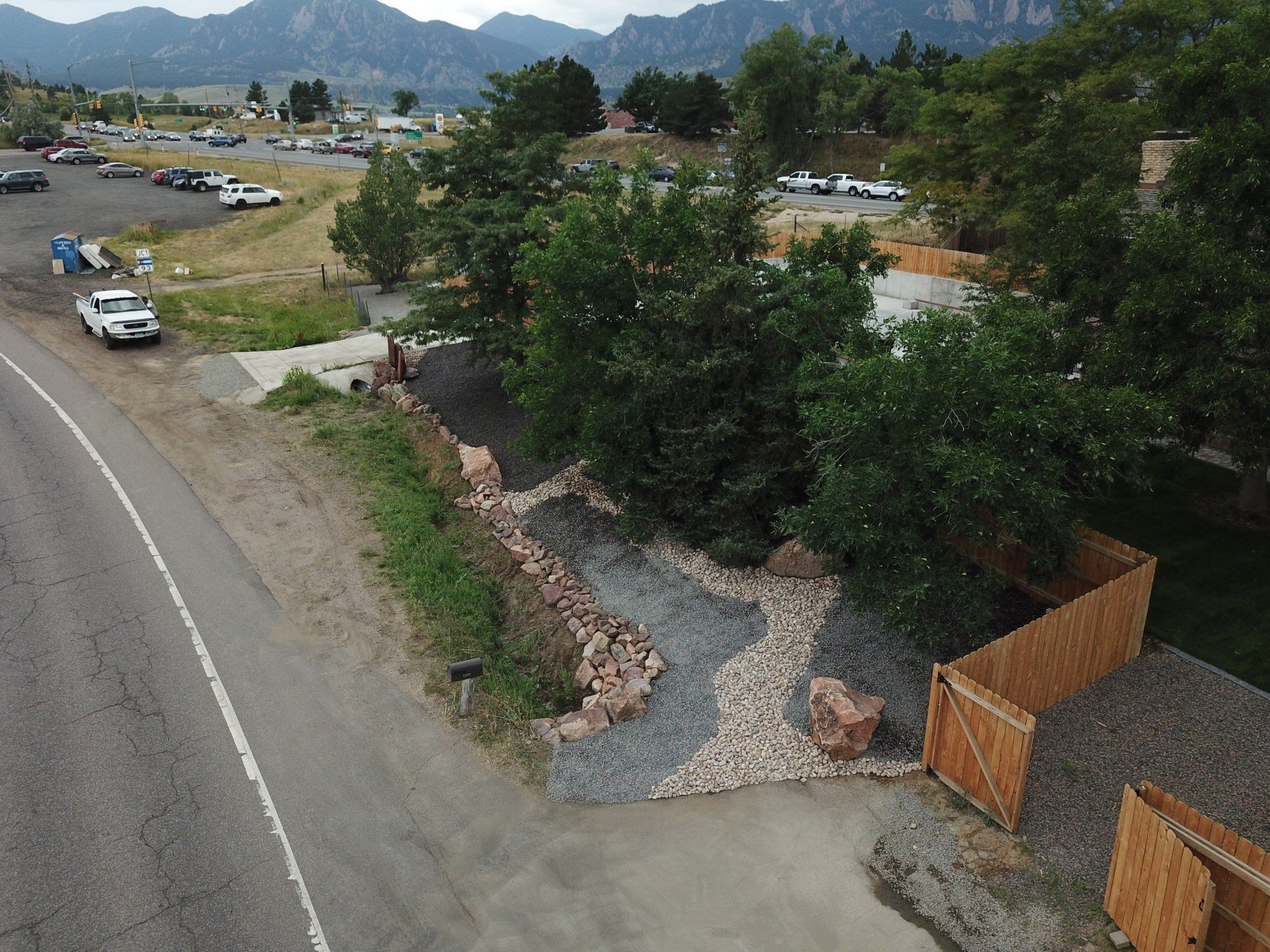 An aerial view of a road, landscaping, and a fenced-in area with mountains in the background.