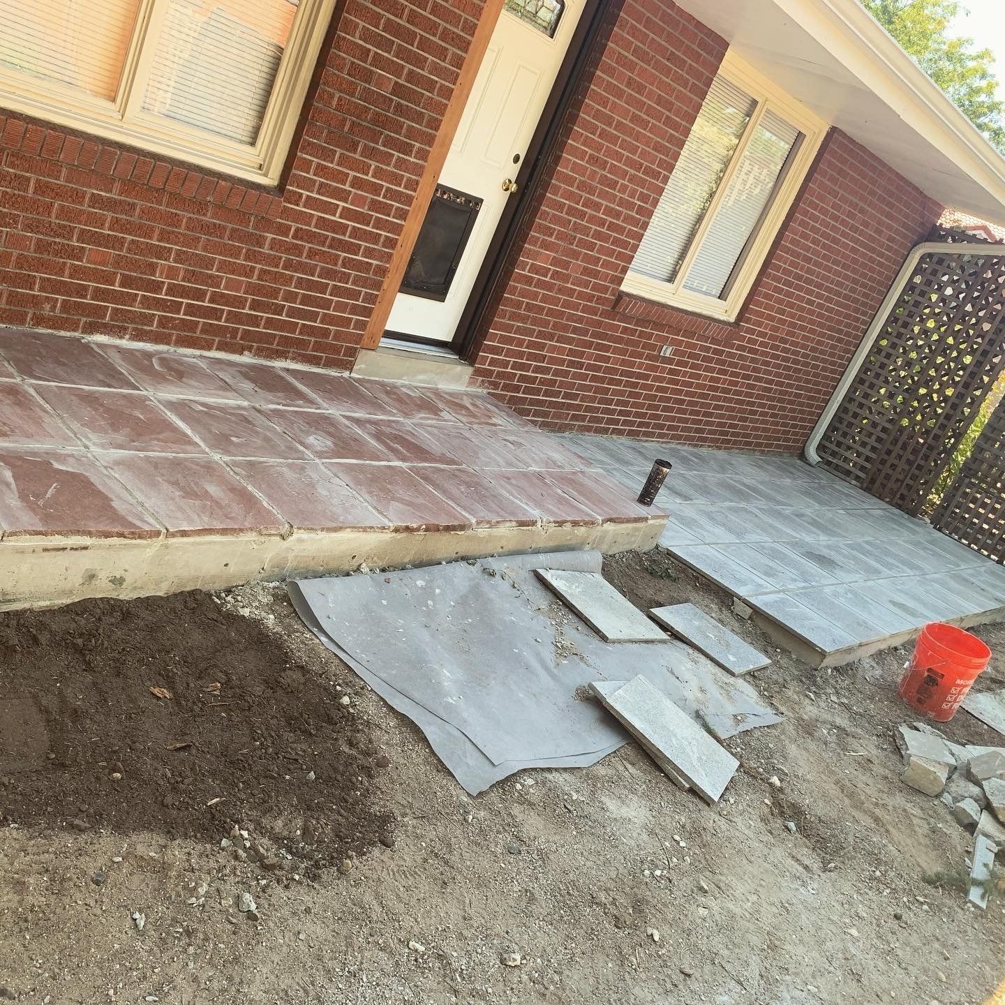 Brick building with patio being built. Ground covered in dirt, gravel, and stone slabs.