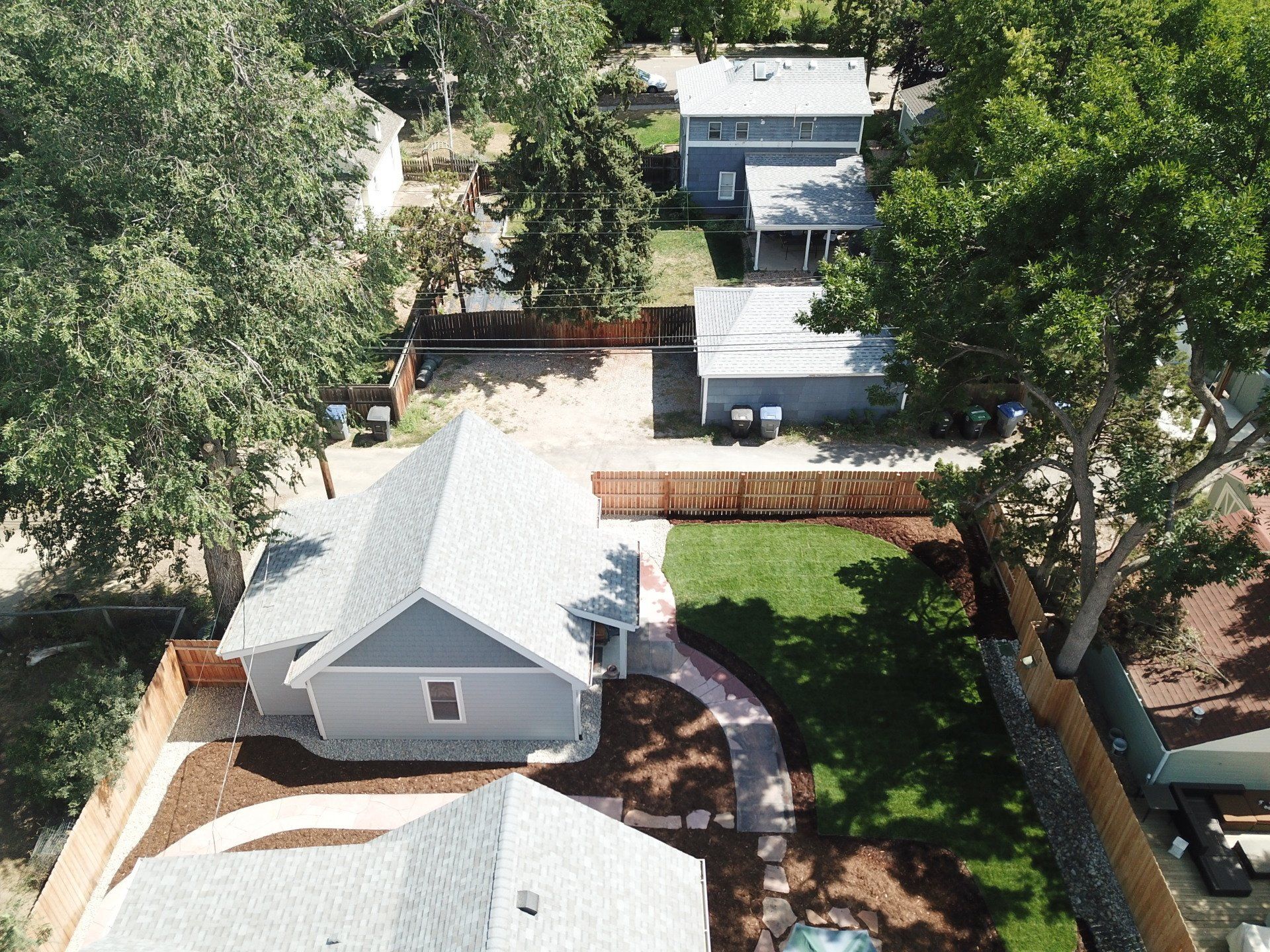 Aerial view of houses with gray siding, green lawns, and wooden fences.