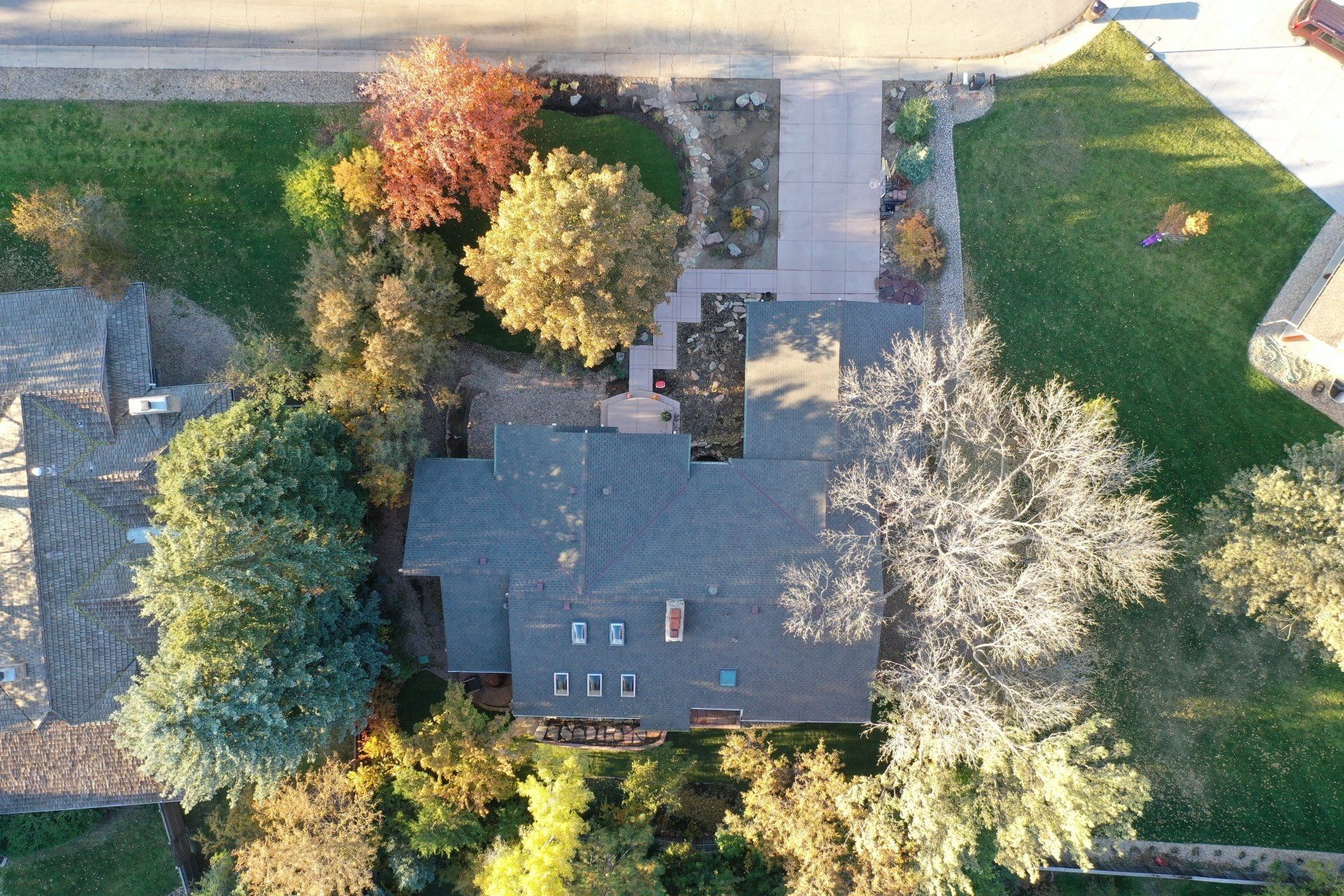 Aerial view of a house surrounded by trees with fall colors, a driveway, and a lawn.
