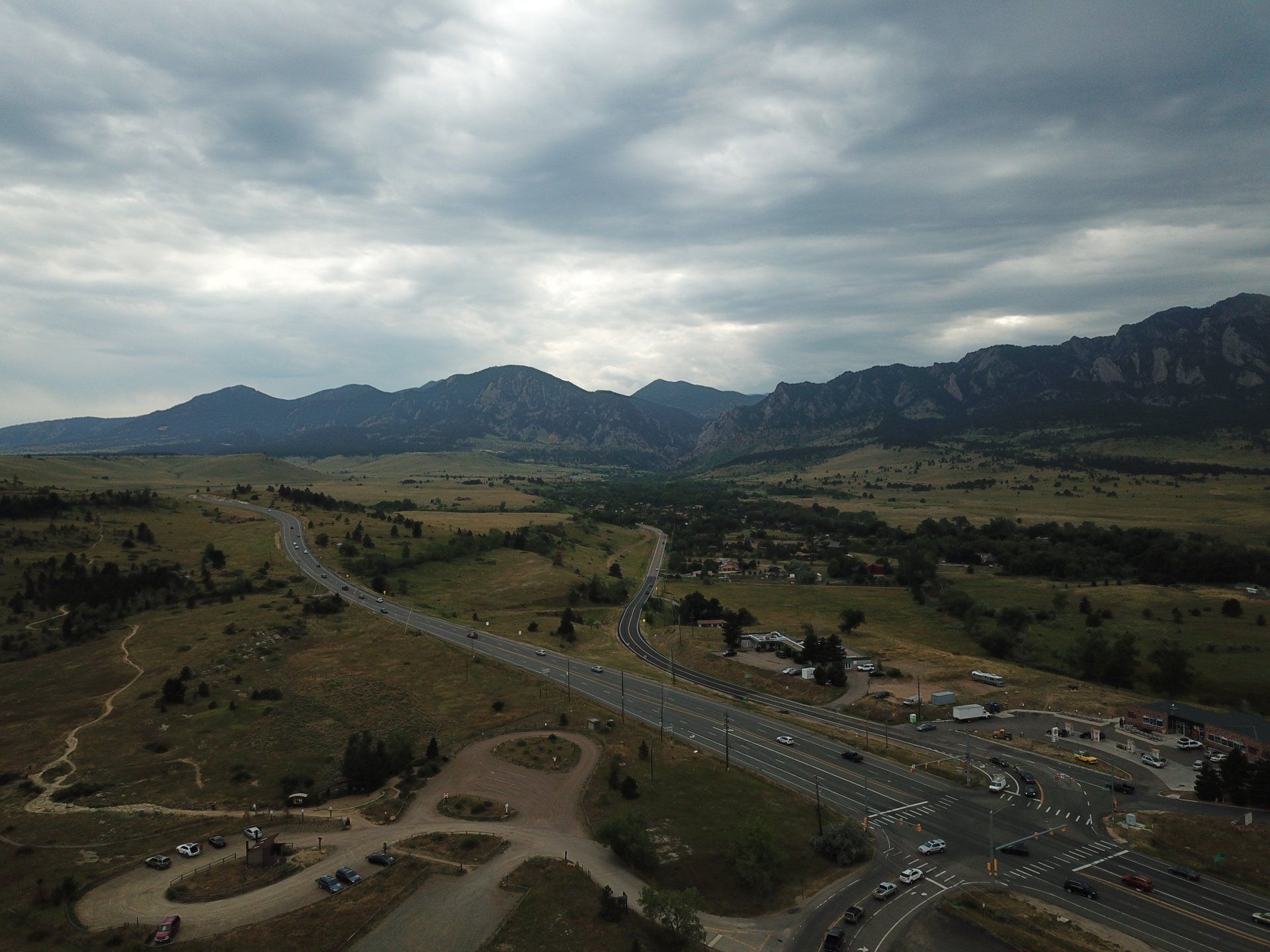 Overhead view of a highway and road leading towards mountains under a cloudy sky.