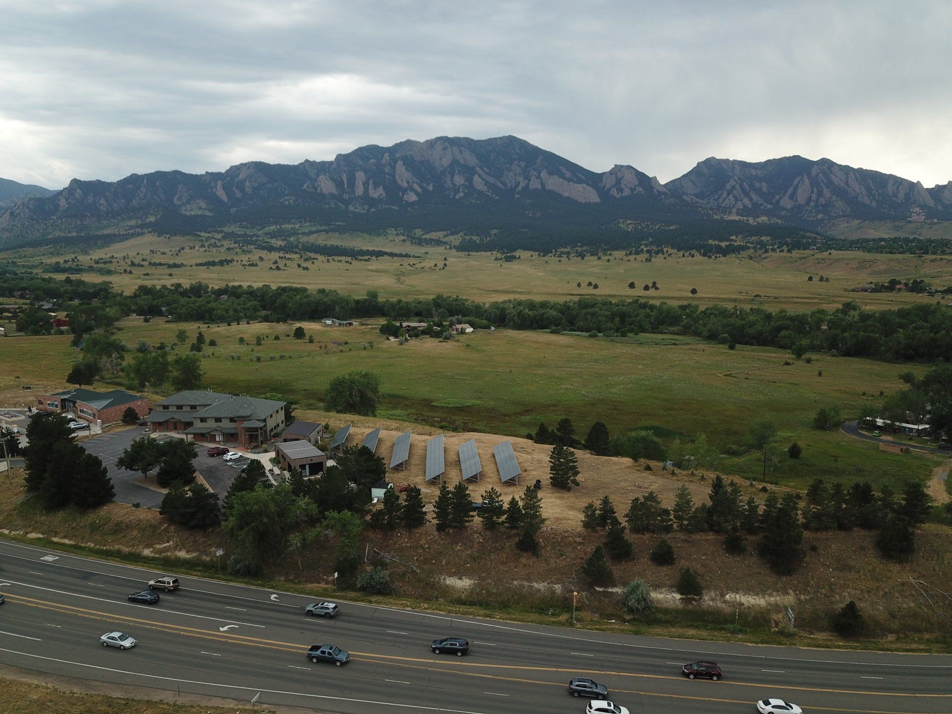 Mountain view with green fields, highway in foreground, buildings, and solar panels.