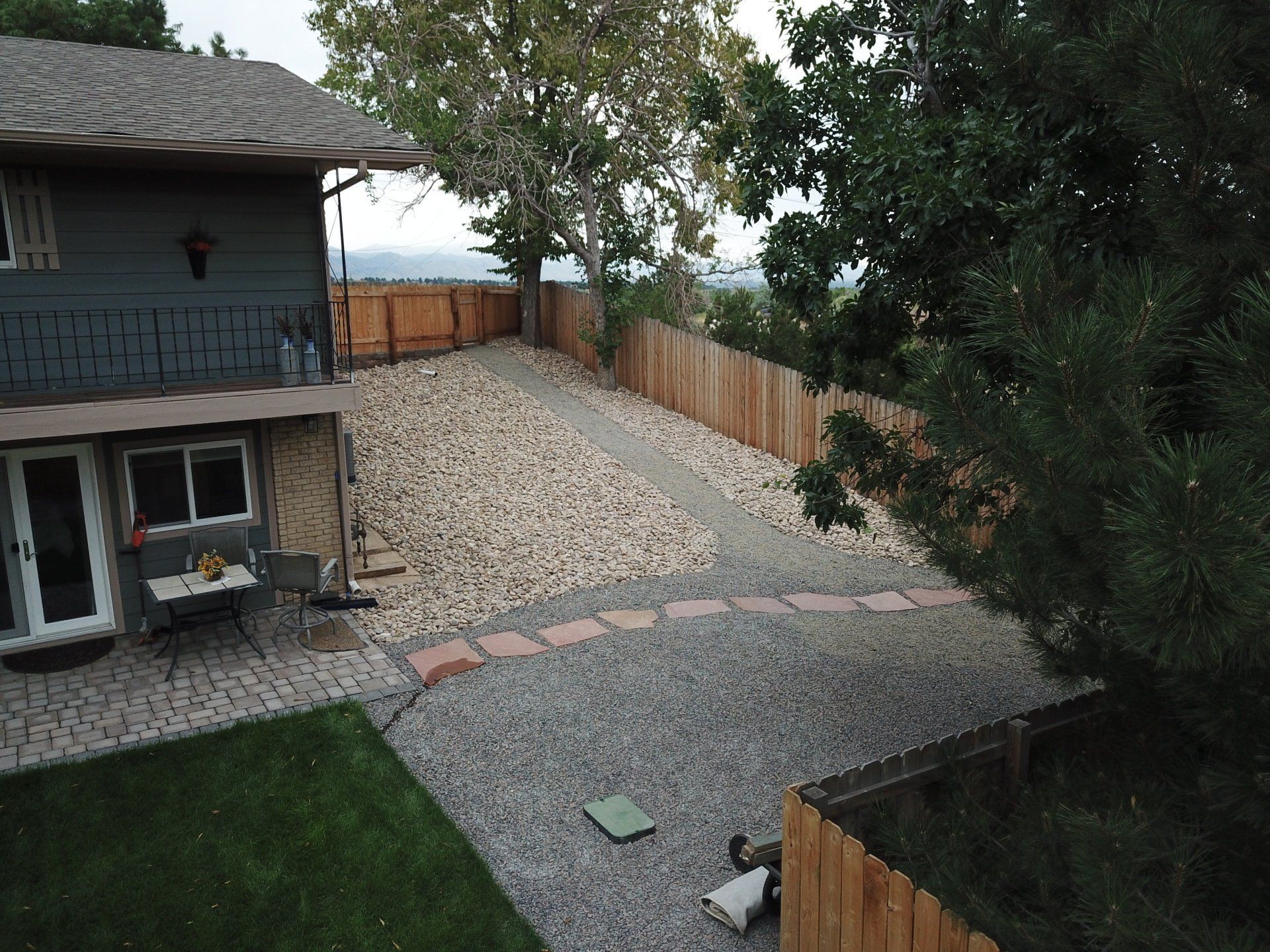 Backyard with gravel path, wooden fence, and house with a green lawn.